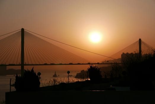 The silhouette of architectural bridge in Hong Kong and ocean at sunset 