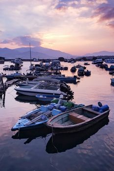 Fishing boats with water reflection in wharf and gradient orange sky at sunset