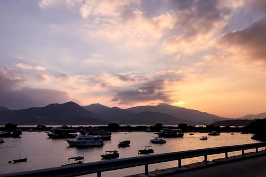 Fishing boats with water reflection in wharf and gradient orange sky at sunset