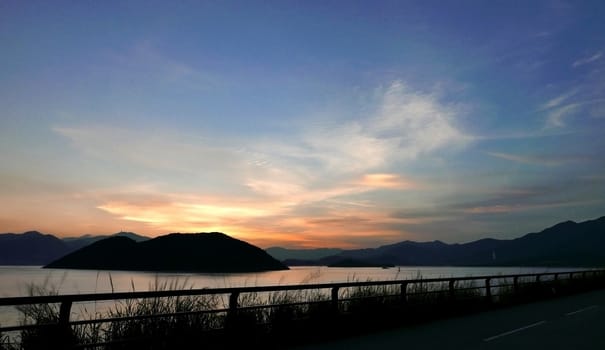 The silhouette of mountain, plant, fence, blue sky and ocean at sunset