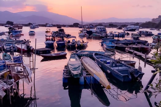 Fishing boats with water reflection in wharf and gradient orange sky at sunset