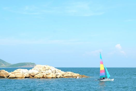 Colorful sailboat passes the small rock island in the sea