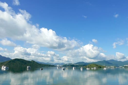 Boats, white clouds, lake and blue sky with reflection shadow