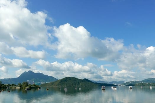 Boats, white clouds, lake and blue sky with reflection shadow