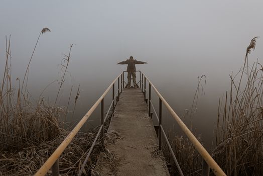 Man with open arms on a frozen pier shrouded in mist