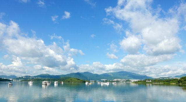 Boats, white clouds, lake and blue sky with reflection shadow