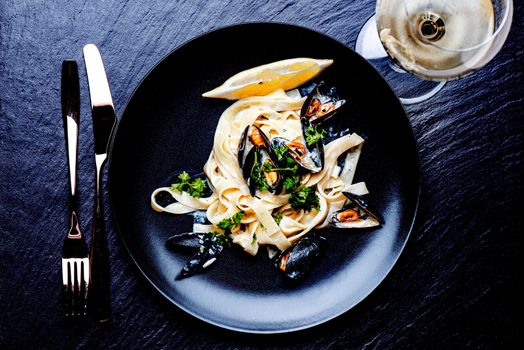 Blue mussels and pasta in black plate on stone surface