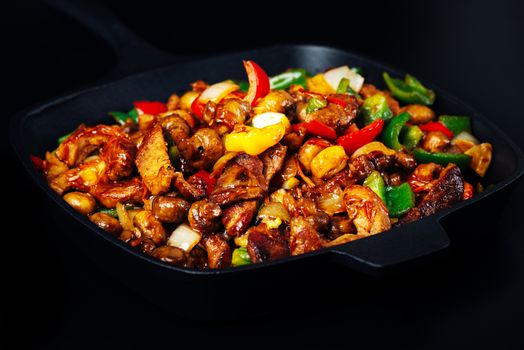 Fried mix of meat and vegetables in cast iron pan on dark background