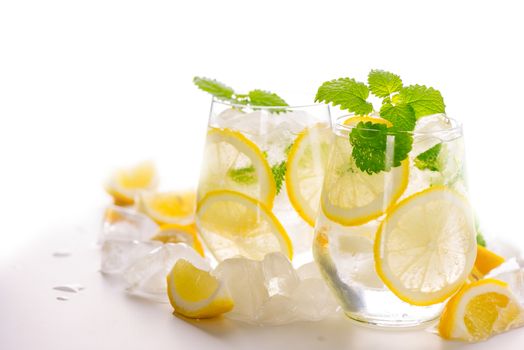 Lemonade drink in a glass: water, ice, lemon slice and mint on white background