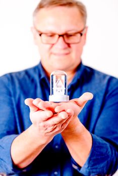 middle aged men in glasses with toy house and  blue shirt