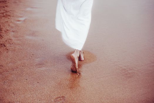 Woman walking on sandy beach in white dress. No face