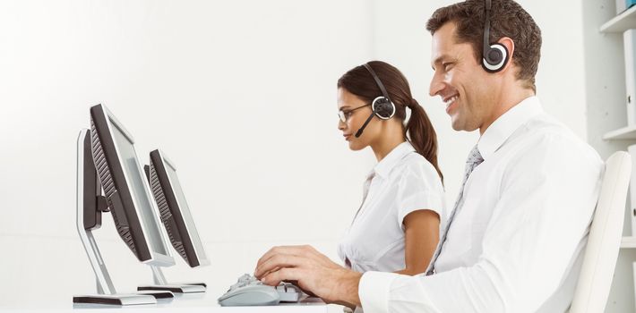 Side view of young business people with headsets using computers in office