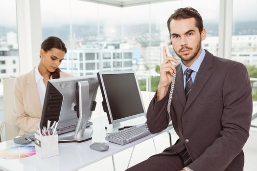 Two young business people using computers in office