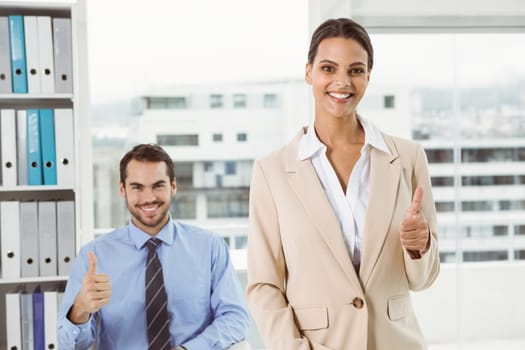 Portrait of two happy business people gesturing thumbs up in office