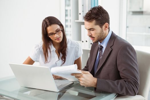 Two young business people using laptop in office