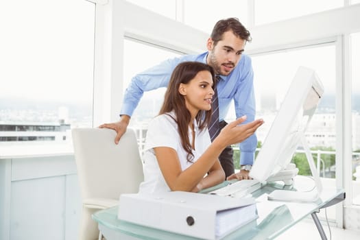 Two young business people using computer in office