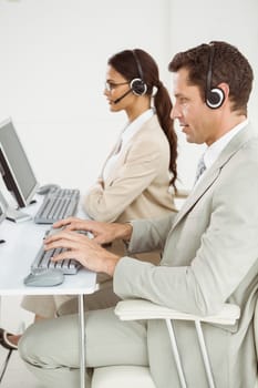 Side view of young business people with headsets using computers in office