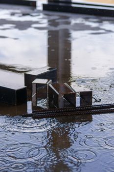 A parts of big square pipes and fixtures under summer rain on construction.