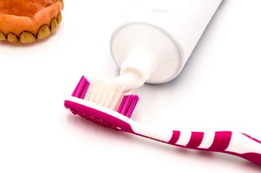 Toothpaste on a toothbrush with a dirty denture on a white background