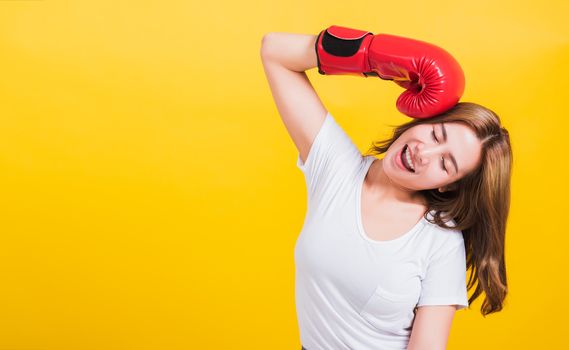 Portrait Asian Thai beautiful young woman standing smile in red boxing gloves punch head and close eyes, shoot the photo in studio shot isolated on yellow background, There was copy space for text