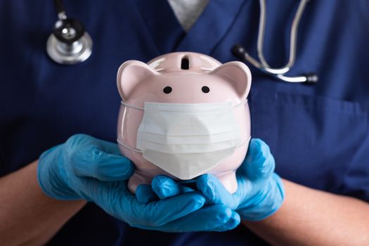 Doctor or Nurse Wearing Surgical Gloves Holding Piggy Bank Wearing Medical Face Mask.