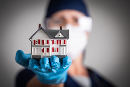Female Doctor or Nurse Wearing Surgical Gloves Holding Model Home.