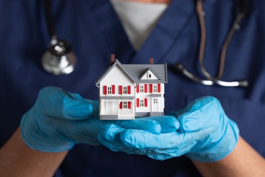 Female Doctor or Nurse Wearing Surgical Gloves Holding Model Home.