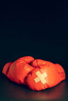 Red boxing gloves in the dark background. Adhesive plaster across each other on boxing gloves. The idea of getting hurt or combat losing business rivals. The idea of fighting giving up boxing.