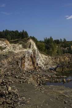 Excavator and basalt columns rocks. Heavy industry. Stone excavation. The excavator produces stone from basalt pillars.