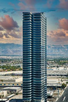 A tall hotel rising from low buildings on the west side of Las Vegas with mountains in the background