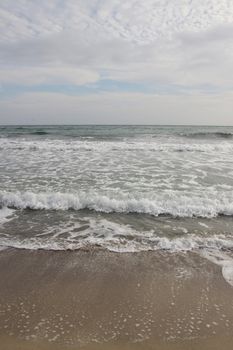 Cloudy weather. Golden sand, waves and foam. Cloudy day on the sandy beach. Panoramic view of beautiful sandy beach. Beach and waves with gloomy sky