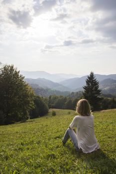 Girl on hiking trip enjoying the sunset view from above. Girl relax and refresh on mountain background is a landscape of high mountains, white clouds. Girl on the mountain looking at the sunny sky.