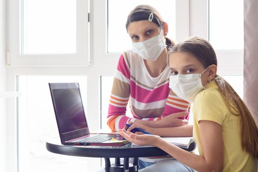 Mom and girl in self-isolation mode are sitting at the table, doing homework and looked into the frame.