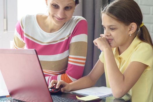 Girl and girl with a smile look at the laptop screen when they see something funny