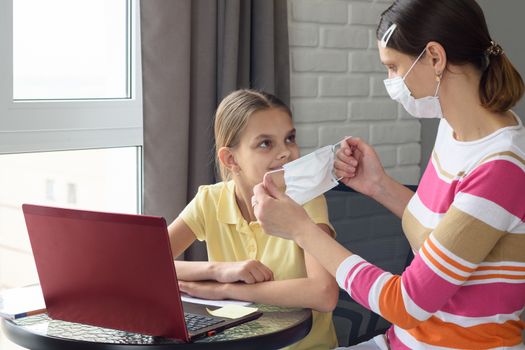 Girl at home puts on protective medical mask to child