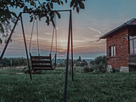 Sunset view in front of a metal swing and an old house.