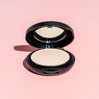 Compact powder on pink background. Female pressed powder in ajar opened black plastic case with mirror, copy space for text or design. Hard light. Square