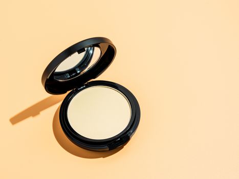 Compact powder on yellow or cream background. Female pressed powder in ajar opened black plastic case with mirror, copy space right for text or design. Hard light. Top view or flat lay