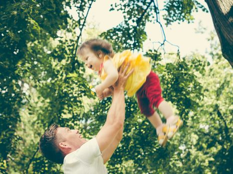 Dad and his little one-year old daughter having fun. Father throws up his little girl. Colorful image for modern life family concept