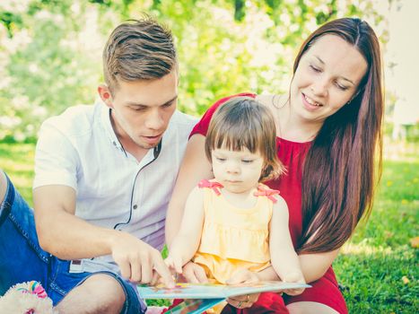 Parents and daughter reading book outdoors on grass at park