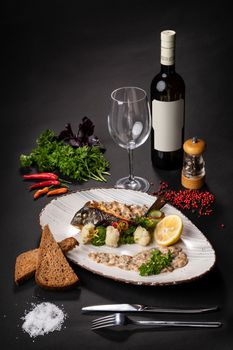 Fish dish on a plate next to a bottle of wine and a glass on a black background