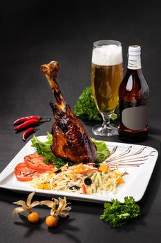 Lamb leg on a plate next to a bottle of beer on a black background