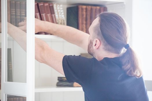 people, knowledge, education and school concept - close up of man taking book from shelf in domestic library