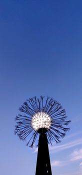 An abstract lamp that looks like a dandelion against the backdrop of a blue evening sky.