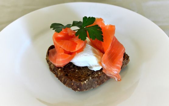 A poached egg and smoked salmon on rye toast with a parsley garnish