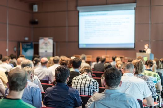 Female speaker giving presentation in lecture hall at university workshop. Audience in conference hall. Rear view of unrecognized participant in audience. Scientific conference event.