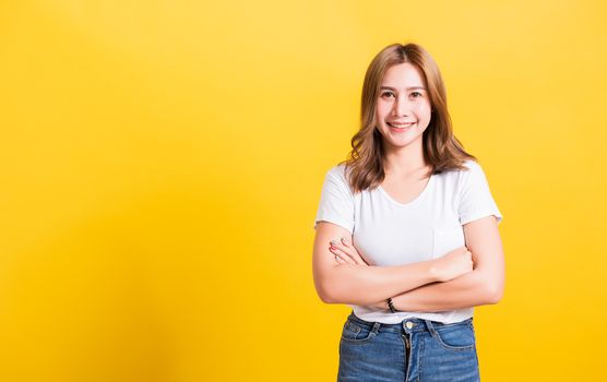 Asian Thai happy portrait beautiful cute young woman standing wear t-shirt her smile confidence with crossed arms looking to camera isolated, studio shot on a yellow background and copy space