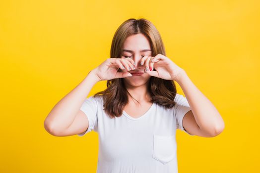 Asian Thai portrait beautiful cute young woman in depressed bad mood her cry wipe tears with fingers, studio shot isolated on yellow background with copy space