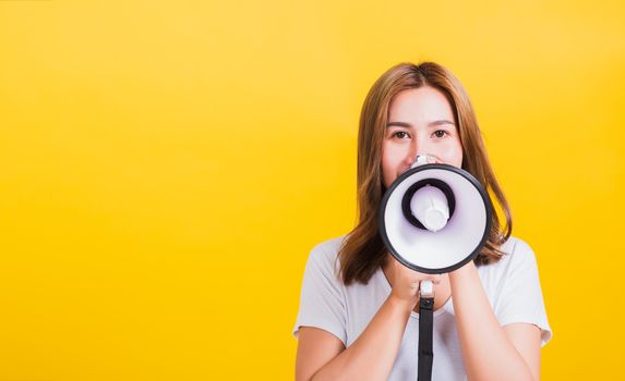 Asian Thai happy portrait beautiful cute young woman standing to make announcement message shouting screaming in megaphone looking to camera, studio shot isolated on yellow background with copy space
