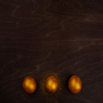 Three big golden easter eggs on dark wooden background copy space for text